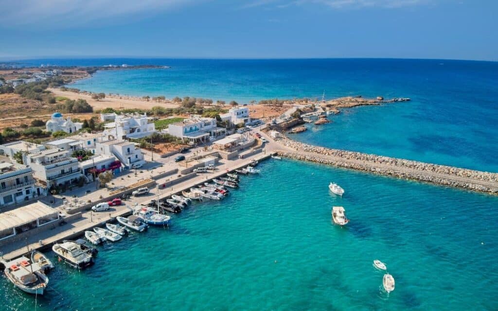 Scenic view of Aliki Beach in Paros, Greece, showcasing the picturesque harbor with fishing boats, whitewashed Cycladic buildings, and turquoise waters under a clear blue sky – perfect for a serene Greek island getaway